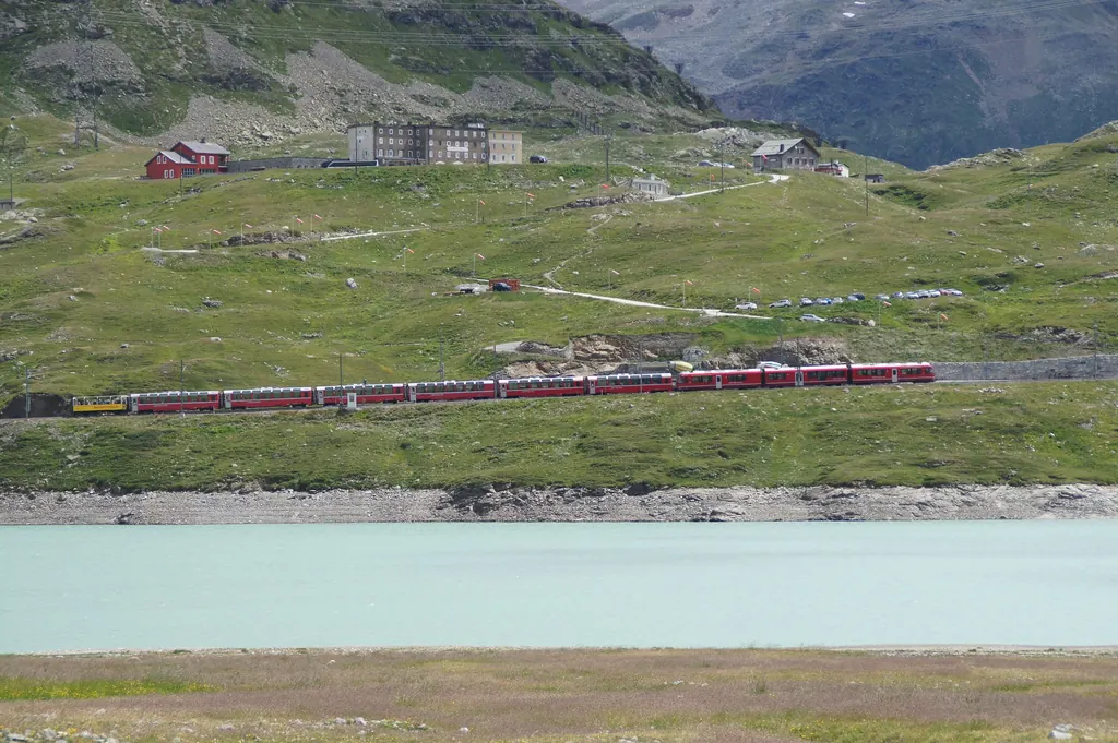 Der Bernina Express mit Panoramawagen fährt am Lago Bianco entlang, am Hang das Hospiz am Berninapass