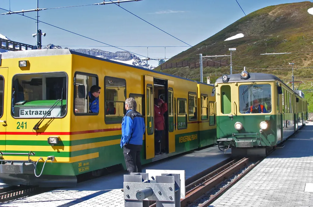 Half price with the Swiss Half Fare Card: Wengernalp Railway trains at Kleine Scheidegg, passengers boarding, green slopes behind
