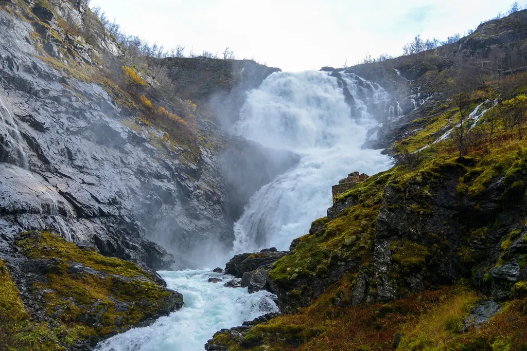 Der Wasserfall Kjosfossen stürzt in mehreren Stufen über dunklen Fels, am Fuß steigt Gischt auf