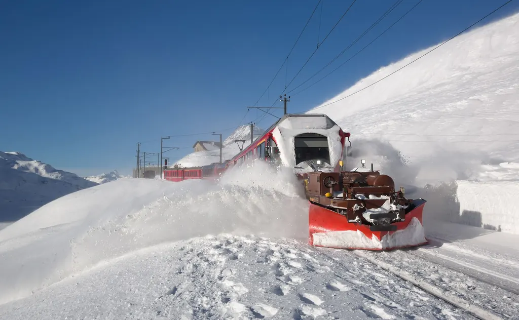 Ein roter Triebzug der Rhätischen Bahn schiebt mit einem Spurpflug Schnee von den Gleisen bei Ospizio Bernina