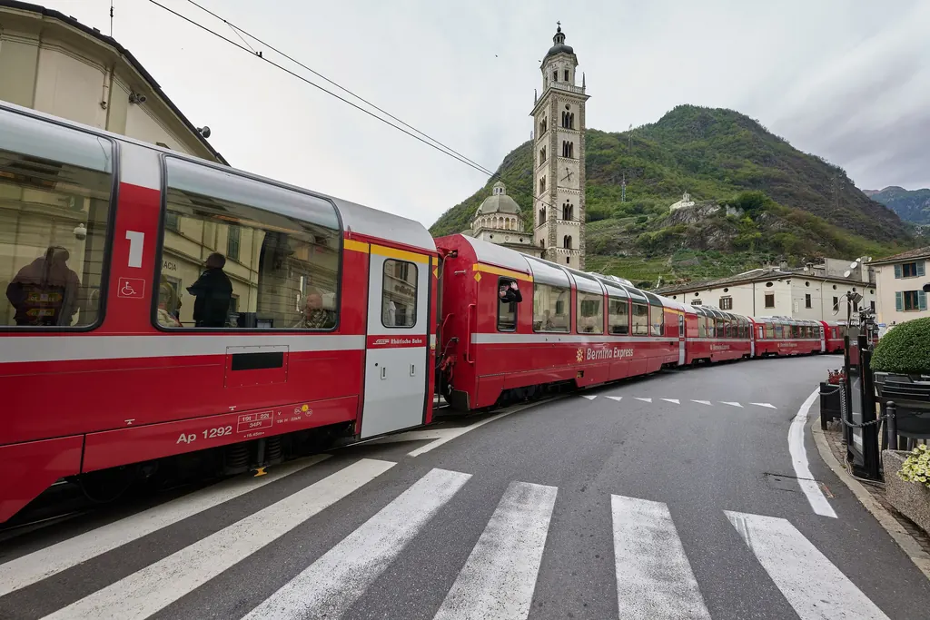 Rote Panoramawagen des Bernina Express fahren in Tirano über den Platz vor der Wallfahrtskirche Madonna di Tirano
