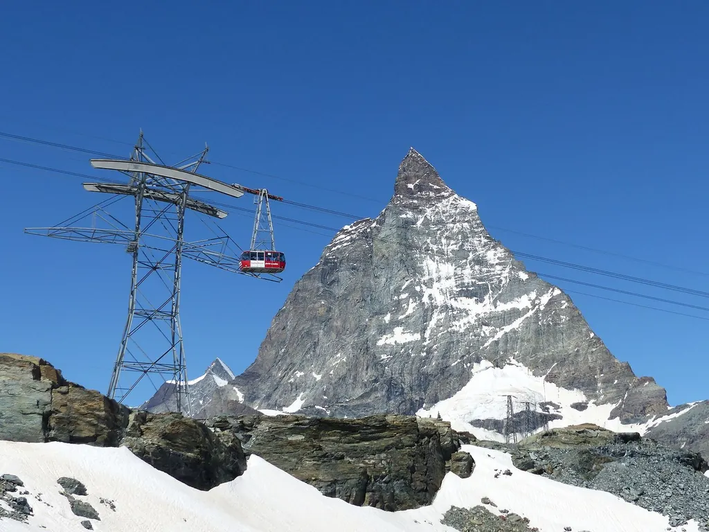 Eine rote Seilbahngondel schwebt an einem Mast vorbei, dahinter die Ostwand des Matterhorns