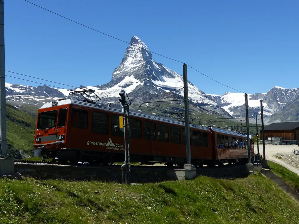 Ein rotbrauner Triebwagen der Gornergrat Bahn steht auf grüner Alpwiese, direkt dahinter ragt das Matterhorn in den blauen Himmel