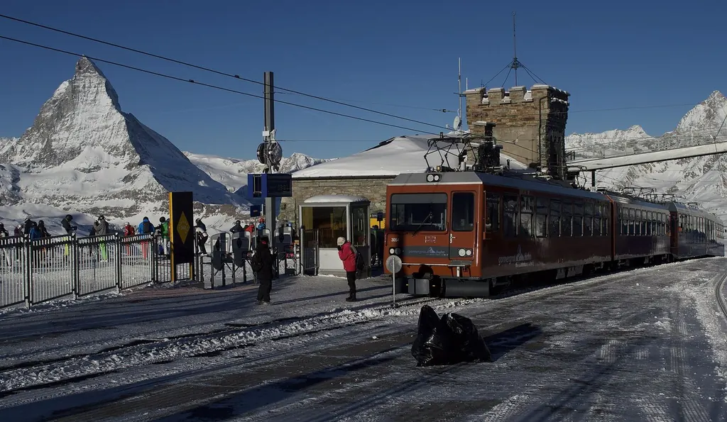 Zwei Züge der Gornergrat Bahn an der verschneiten Bergstation, links dahinter das Matterhorn unter wolkenlosem Himmel
