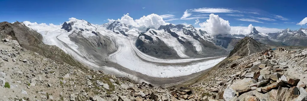 Weites Panorama vom Gornergrat: links das vergletscherte Monte-Rosa-Massiv, in der Mitte der geschwungene Gornergletscher, rechts das Matterhorn mit einer Wolkenfahne