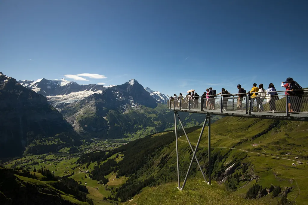Besucher stehen auf der Aussichtsplattform des First Cliff Walk, die auf Stahlstützen über den Hang ragt; tief unten das Tal von Grindelwald, dahinter Gletscher und Gipfel