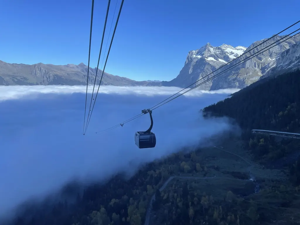 Eine Kabine des Eiger Express an drei Seilen über einem Nebelmeer, dahinter ein vergletscherter Gipfel in der Morgensonne