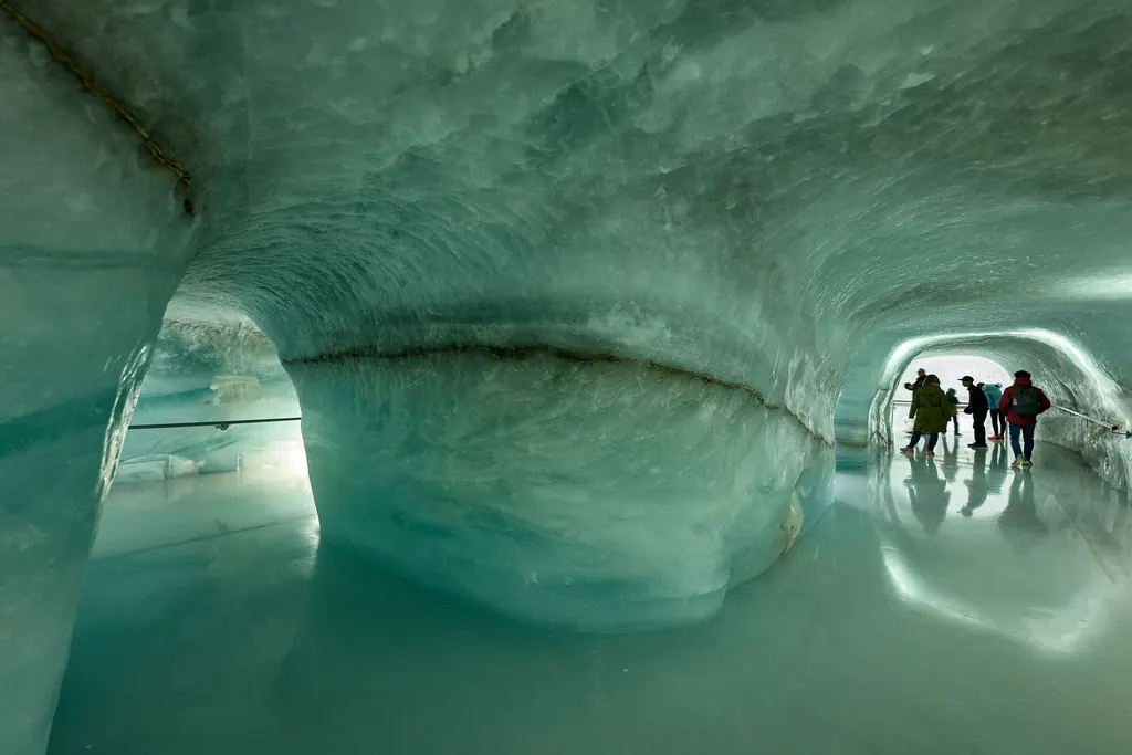Besucher in einem grünlich schimmernden, glatt geschliffenen Gang des Eispalasts im Gletscher unter dem Jungfraujoch