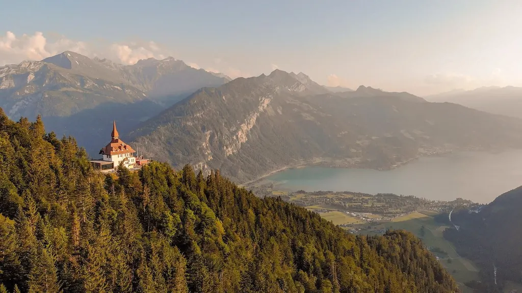 Das Restaurant Harder Kulm auf dem bewaldeten Grat über Interlaken, dahinter der Thunersee im Abendlicht