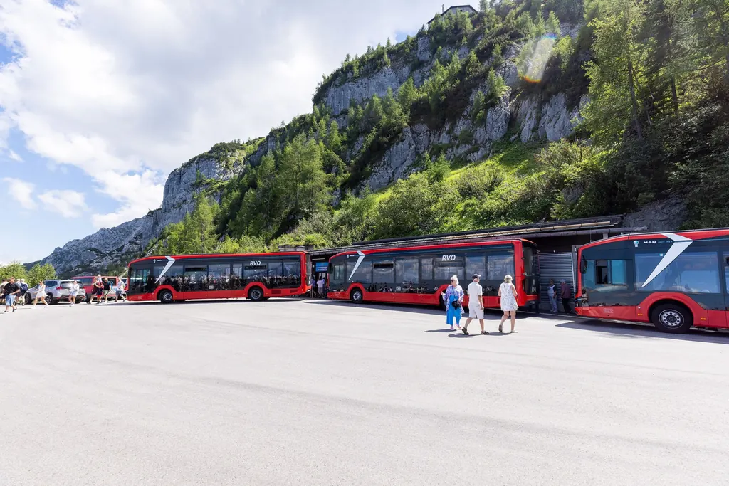 Three red buses of the Kehlstein line on the turning area beneath the rock face of the Kehlstein, a few passengers in front of them
