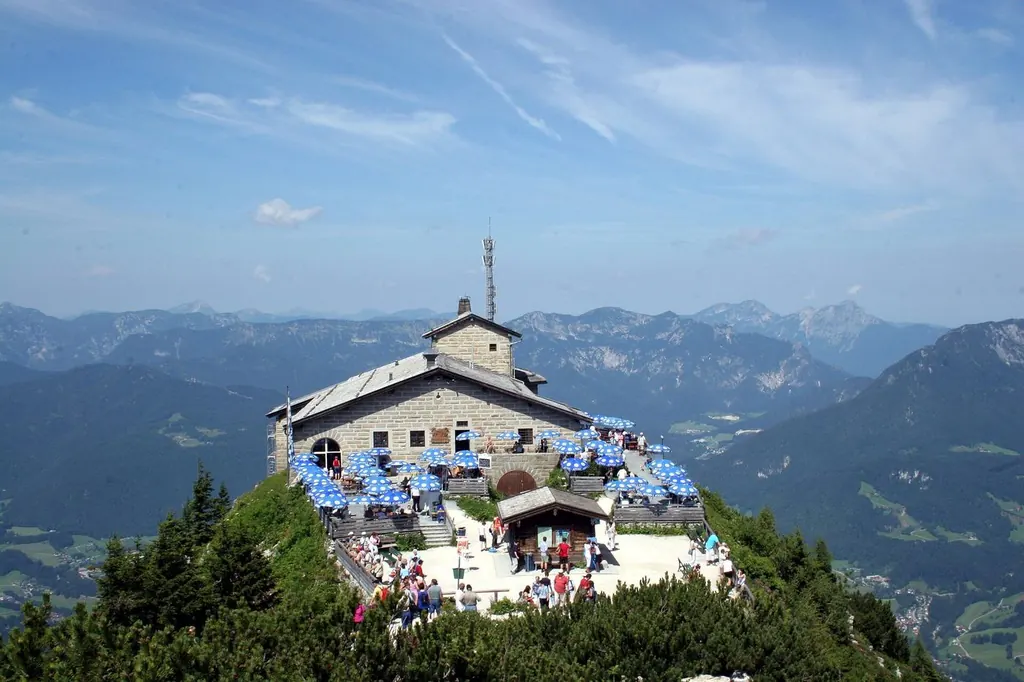 Das Kehlsteinhaus bei klarer Sicht, volle Sonnenterrasse, dahinter Bergketten bis zum Horizont