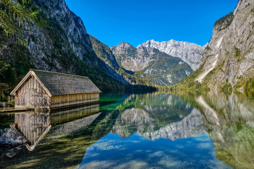 Ein hölzernes Bootshaus am spiegelglatten Obersee, dahinter steile Felswände und verschneite Gipfel