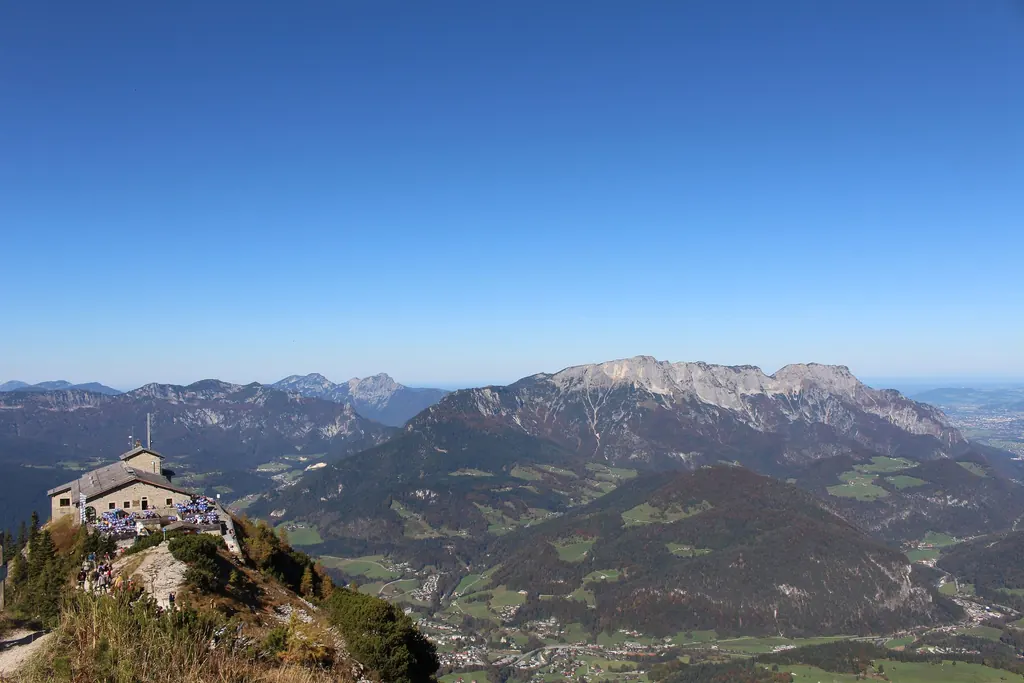 Wide view from the Kehlstein: bottom left the Eagle's Nest small on the ridge, behind it the Untersberg and the Salzburg basin under a cloudless sky