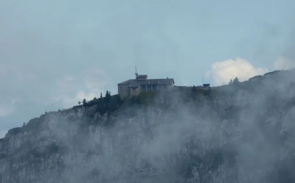 Das Kehlsteinhaus auf dem Grat, von Wolkenfetzen umgeben, darunter die dunkle Felswand