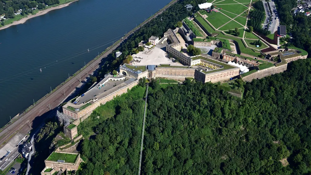 Luftbild der Festung Ehrenbreitstein auf ihrem Felssporn hoch über dem Rhein, links der Fluss, ringsum bewaldete Hänge