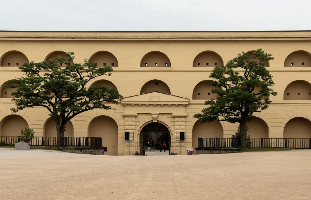 Der Innenhof der Festung mit der langen gelblichen Kasernenfassade, einer Reihe von Rundbögen und zwei Bäumen davor