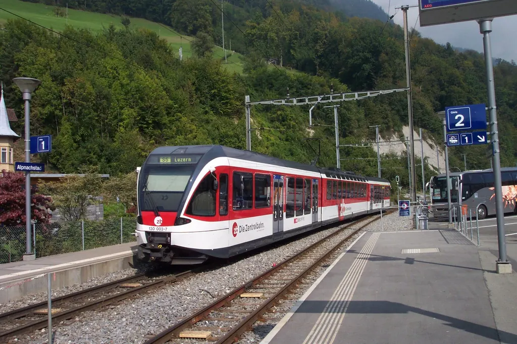 A red and white Zentralbahn train stands at Alpnachstad station, the wooded slope of Pilatus behind it