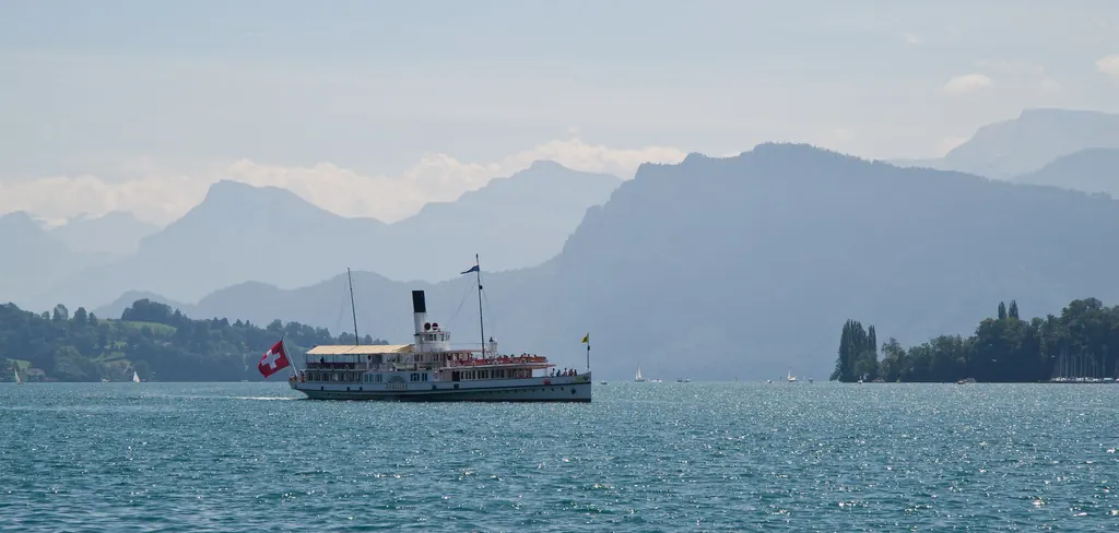 Ein weißer Raddampfer mit Schweizer Flagge fährt über den Vierwaldstättersee, dahinter die Bergkulisse