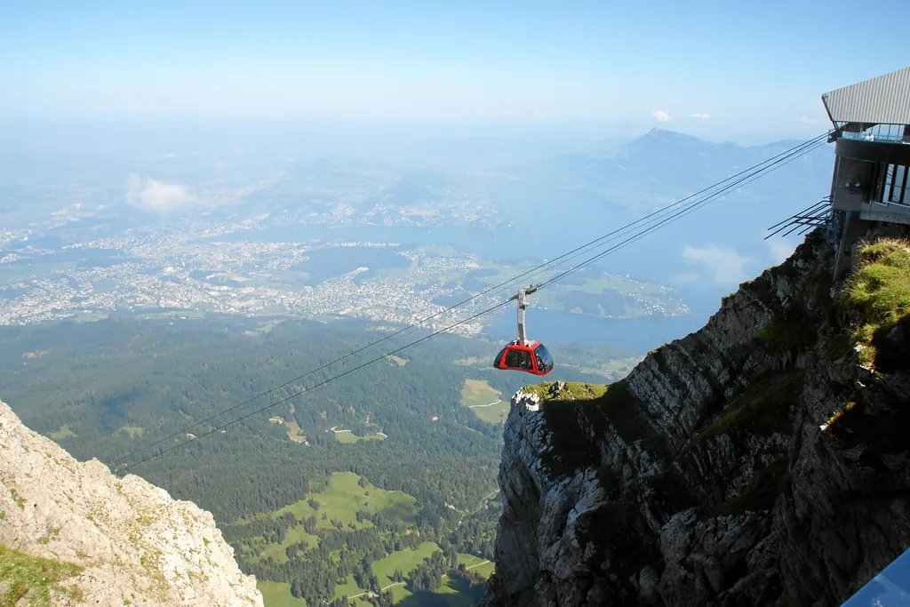 Eine rote Kabine der Luftseilbahn Dragon Ride hängt vor der Bergstation über dem Abgrund, tief unten der Vierwaldstättersee und Luzern
