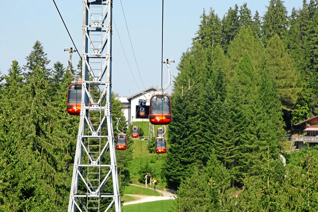 Rote 4er-Gondeln der Panorama-Gondelbahn fahren zwischen Tannen an einer Stütze vorbei