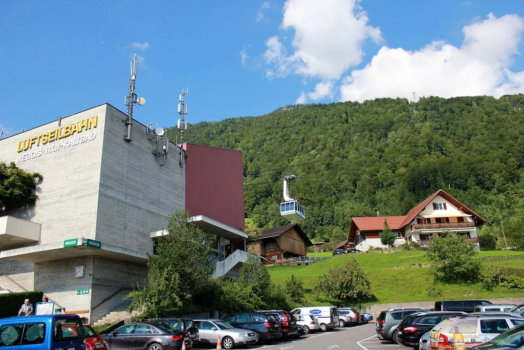 The valley station of the Weggis – Rigi Kaltbad cable car with a cabin above the car park, the wooded slope behind