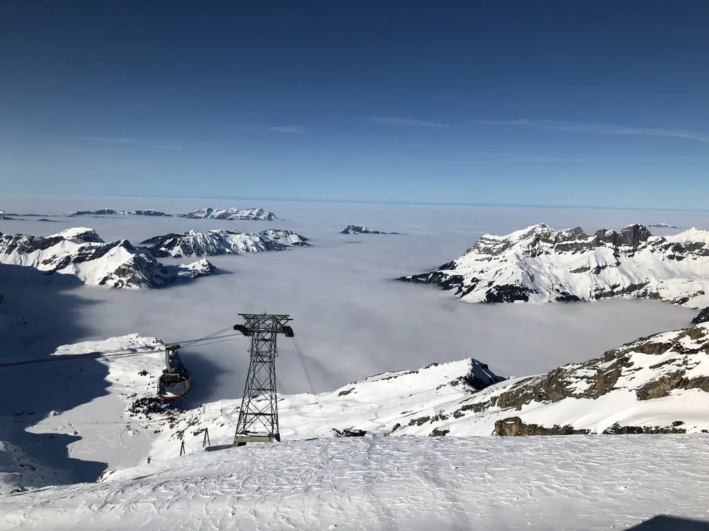 Die Kabine der TITLIS Rotair hängt an der Stütze über einem Nebelmeer, dahinter die schneebedeckten Gipfel der Zentralschweiz