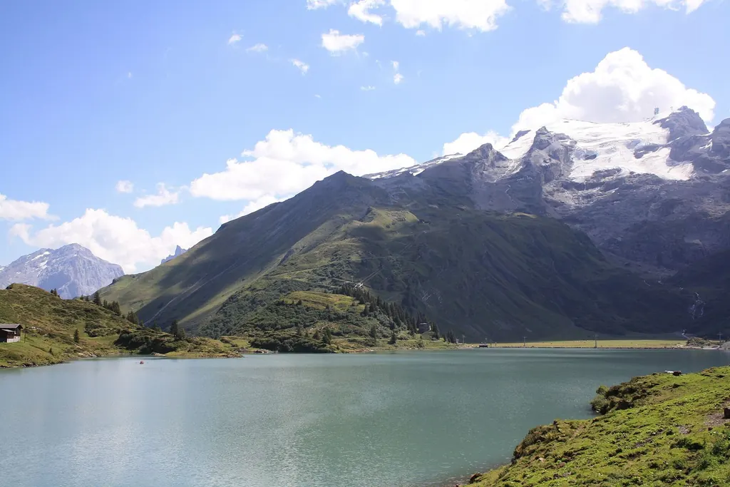 Der Trübsee liegt grün unter dem Titlis, dahinter Gletscher und Felswände, im Vordergrund die Wiese am Ufer