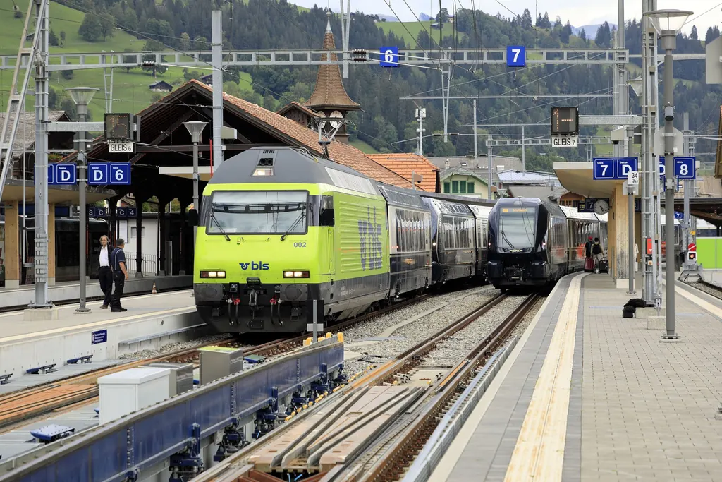 The GoldenPass Express with a green BLS locomotive stands at Zweisimmen station, wooded hills of the Simmental behind