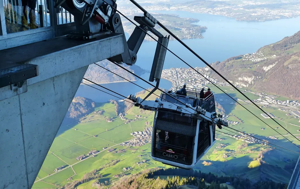 The open-top CabriO cable car of the Stanserhorn railway floats high above Lake Lucerne, passengers standing in the open air on the upper deck
